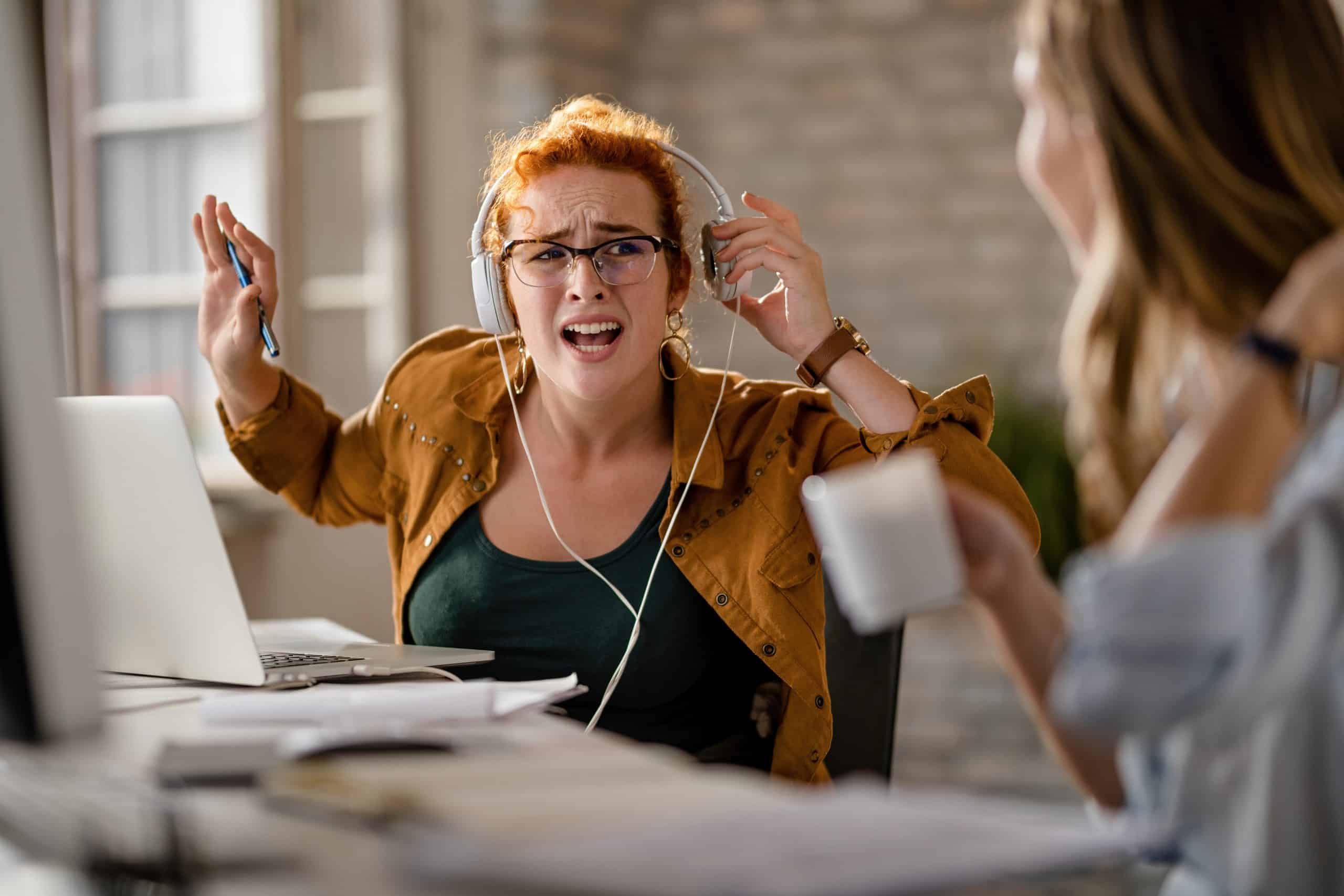Una estudiante de inglés con cascos quitándose uno para escuchar mejor, con una expresión de confusión, como diciendo "¿Eh?".